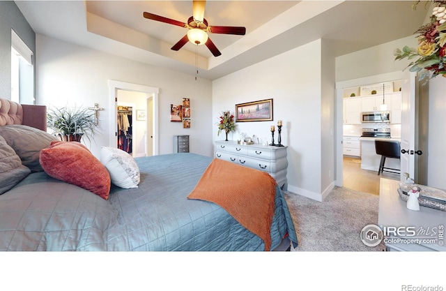 bedroom featuring a spacious closet, light colored carpet, ceiling fan, and a tray ceiling