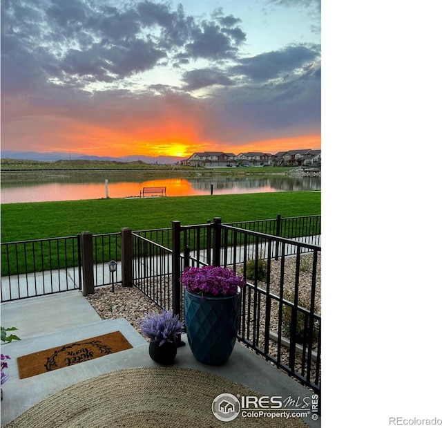 patio terrace at dusk featuring a water view and a yard