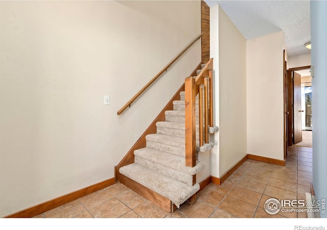 stairs with tile patterned flooring, baseboards, and a textured ceiling