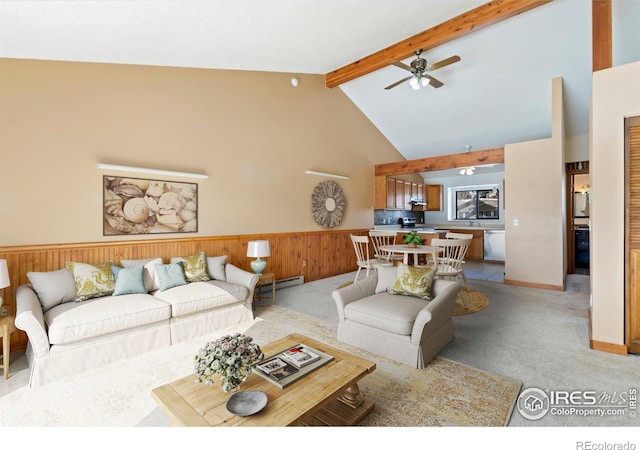 living room featuring beamed ceiling, light carpet, high vaulted ceiling, wooden walls, and wainscoting