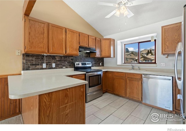 kitchen featuring a peninsula, a sink, stainless steel appliances, vaulted ceiling, and under cabinet range hood