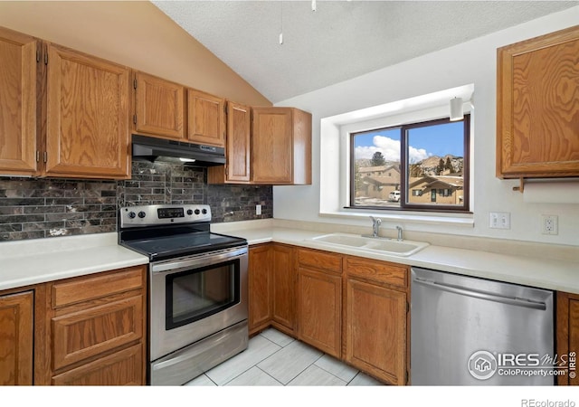 kitchen featuring under cabinet range hood, light countertops, lofted ceiling, appliances with stainless steel finishes, and a sink