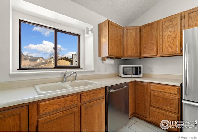 kitchen with lofted ceiling, a sink, stainless steel appliances, a textured ceiling, and brown cabinets