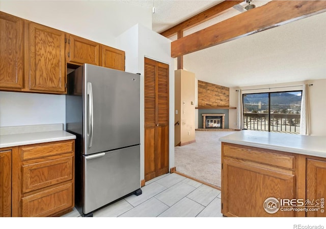 kitchen with a large fireplace, open floor plan, light countertops, brown cabinets, and freestanding refrigerator