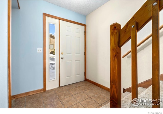 tiled entryway with baseboards and a textured ceiling