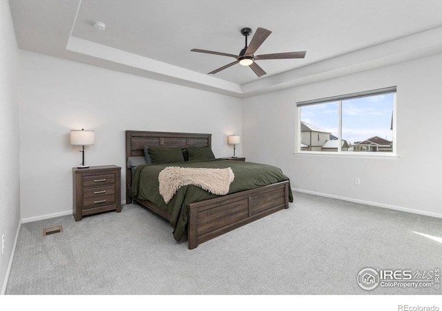 bedroom with light colored carpet, a raised ceiling, and ceiling fan