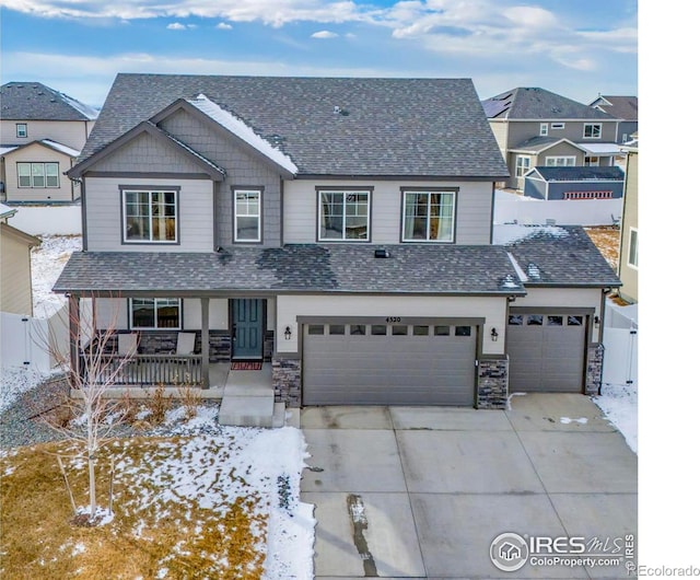 view of front of property with stone siding, covered porch, concrete driveway, and fence