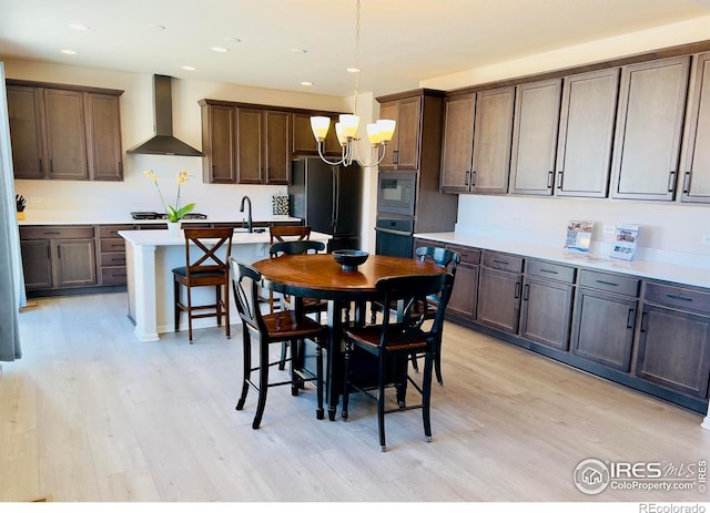 kitchen with light wood finished floors, wall chimney range hood, hanging light fixtures, a notable chandelier, and black appliances