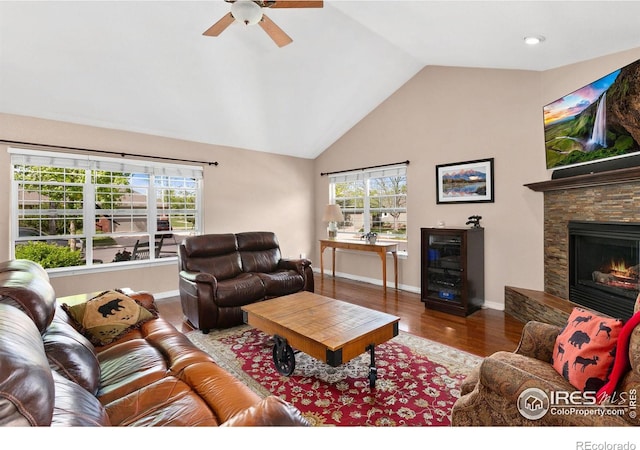 living room with wood-type flooring, a stone fireplace, plenty of natural light, and lofted ceiling