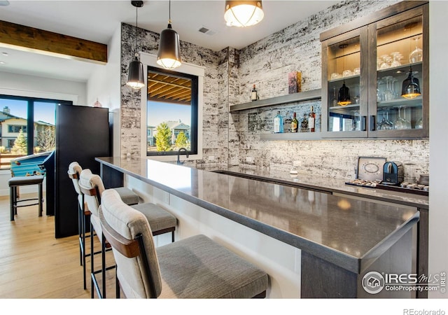 bar featuring light wood-type flooring, pendant lighting, and beamed ceiling