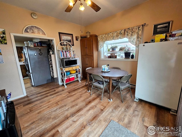 dining space featuring a ceiling fan, vaulted ceiling, baseboards, and wood finished floors