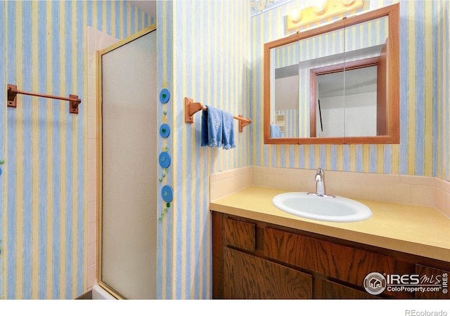 bathroom featuring a shower with door, vanity, and wallpapered walls