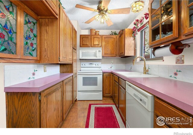 kitchen with white appliances, brown cabinetry, a sink, and glass insert cabinets