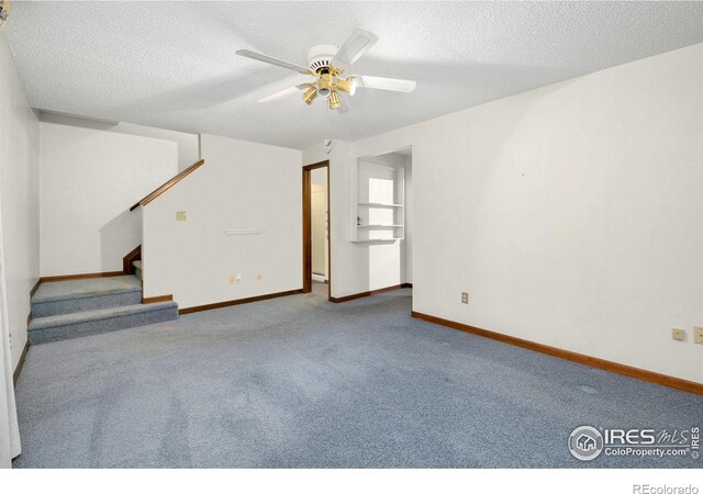 unfurnished living room featuring carpet, stairway, a ceiling fan, a textured ceiling, and baseboards