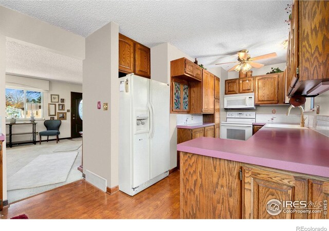 kitchen with white appliances, brown cabinets, wood finished floors, a peninsula, and a sink