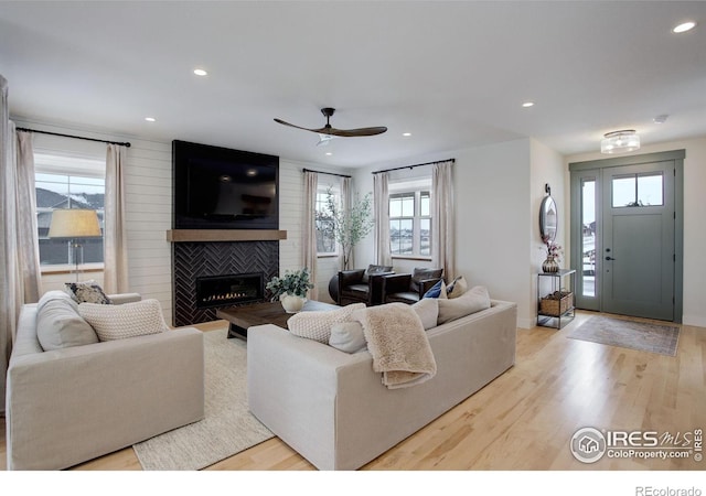 living room featuring light wood-type flooring, ceiling fan, and a fireplace