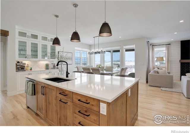 kitchen featuring a center island with sink, hanging light fixtures, sink, stainless steel dishwasher, and white cabinets