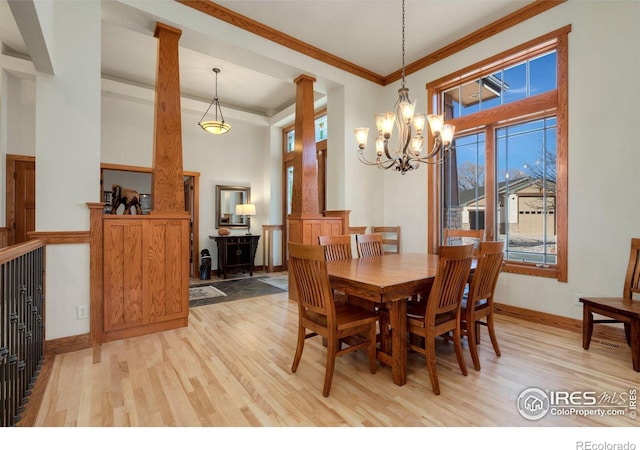 dining area with a towering ceiling, a chandelier, ornamental molding, light wood-type flooring, and ornate columns