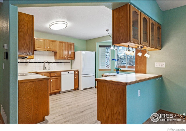 kitchen featuring light hardwood / wood-style flooring, white appliances, decorative backsplash, sink, and kitchen peninsula