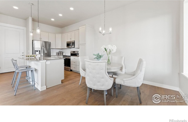 kitchen with decorative backsplash, stainless steel appliances, a kitchen bar, white cabinetry, and a notable chandelier