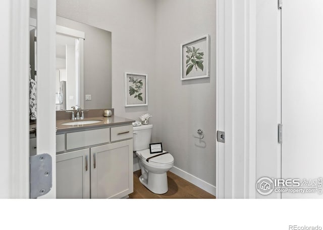 bathroom featuring toilet, baseboards, wood finished floors, and vanity