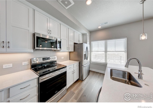 kitchen with sink, white cabinets, stainless steel appliances, and hanging light fixtures