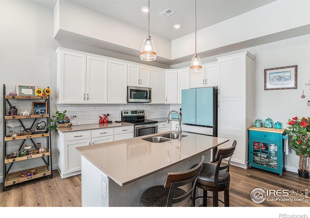 kitchen with a kitchen bar, sink, white cabinetry, stainless steel appliances, and hanging light fixtures