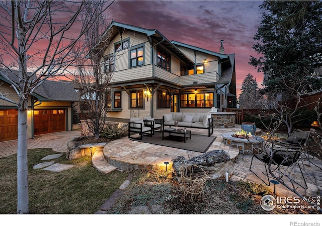 back of house at dusk with a garage, a patio area, an outdoor living space with a fire pit, and a balcony