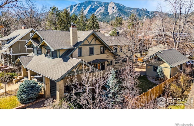 exterior space featuring a shingled roof, a chimney, a mountain view, and fence