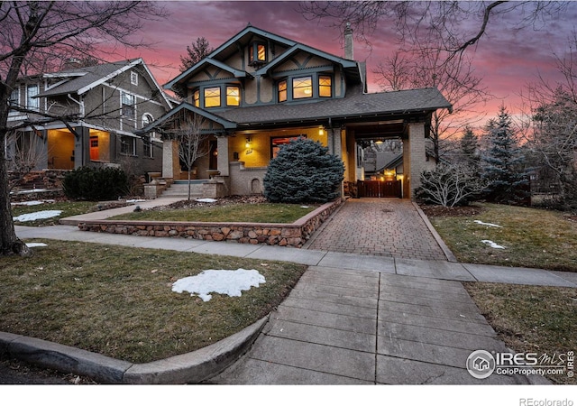 view of front facade featuring decorative driveway, brick siding, a yard, and roof with shingles