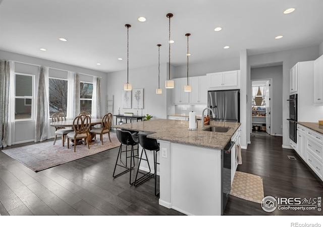 887 Sundance Ln, Erie, CO 80516 - kitchen with stainless steel fridge, dark wood-style flooring, a center island with sink, a kitchen breakfast bar, and white cabinets