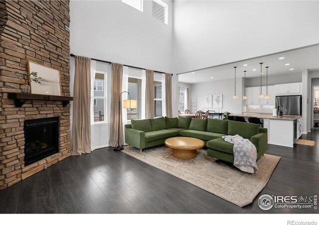 887 Sundance Ln, Erie, CO 80516 - living room featuring a stone fireplace, dark wood-style floors, a towering ceiling, plenty of natural light, and recessed lighting