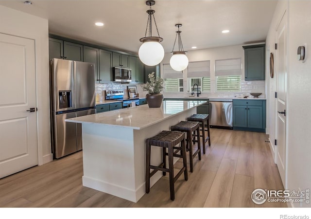 kitchen featuring light wood-type flooring, a center island, decorative light fixtures, light stone counters, and appliances with stainless steel finishes