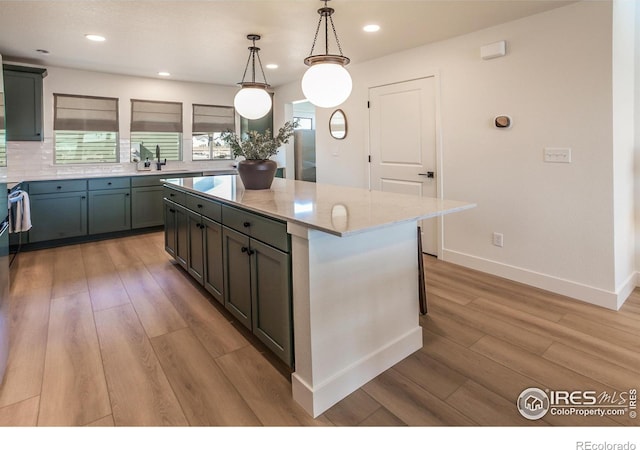 kitchen featuring light hardwood / wood-style flooring, a center island, hanging light fixtures, light stone countertops, and tasteful backsplash