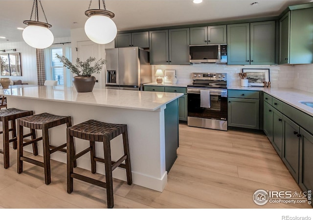 kitchen featuring a kitchen bar, stainless steel appliances, hanging light fixtures, light stone countertops, and tasteful backsplash