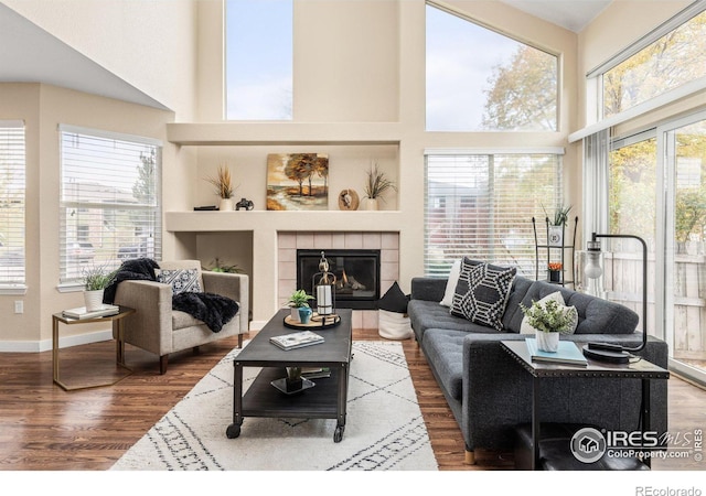 living area featuring a towering ceiling, plenty of natural light, wood finished floors, and a tiled fireplace