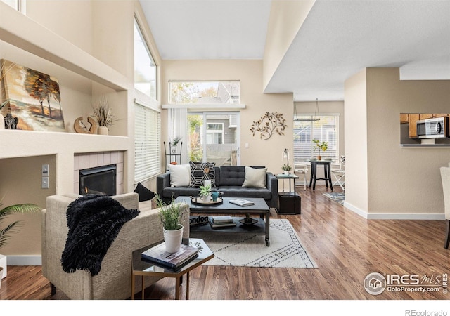 living room with a healthy amount of sunlight, a tile fireplace, baseboards, and wood finished floors