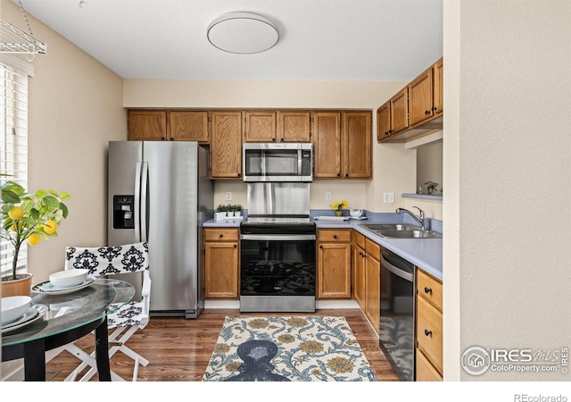 kitchen with brown cabinets, appliances with stainless steel finishes, dark wood-type flooring, and a sink