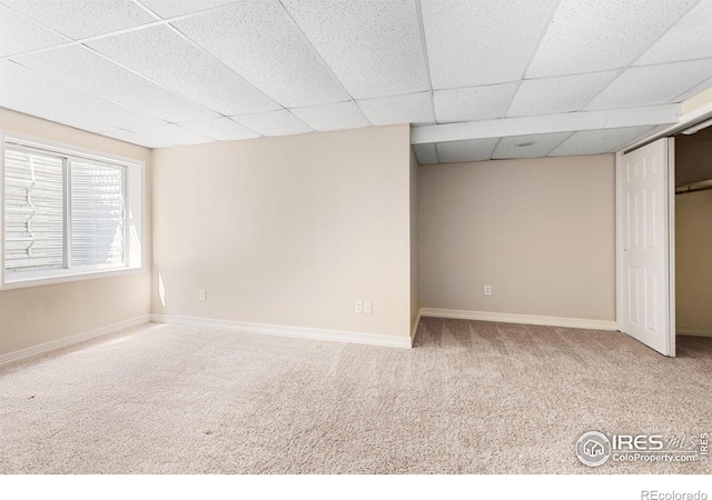 empty room featuring a paneled ceiling, baseboards, and carpet floors