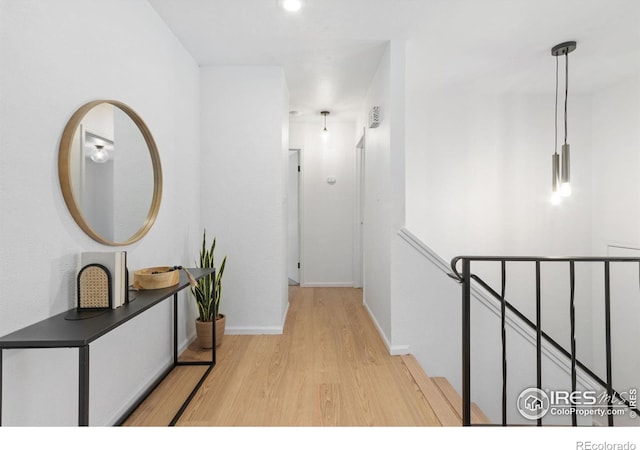 corridor featuring light wood-style flooring, an upstairs landing, and baseboards