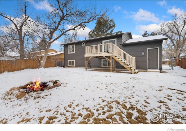 snow covered back of property with an outdoor fire pit, fence, a wooden deck, and stairs