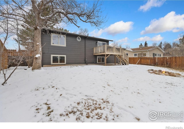 snow covered house with stairs, fence, and a deck