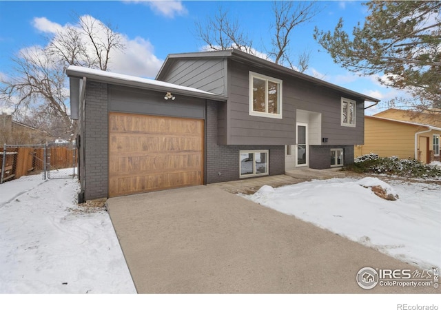 raised ranch with an attached garage, driveway, fence, and brick siding