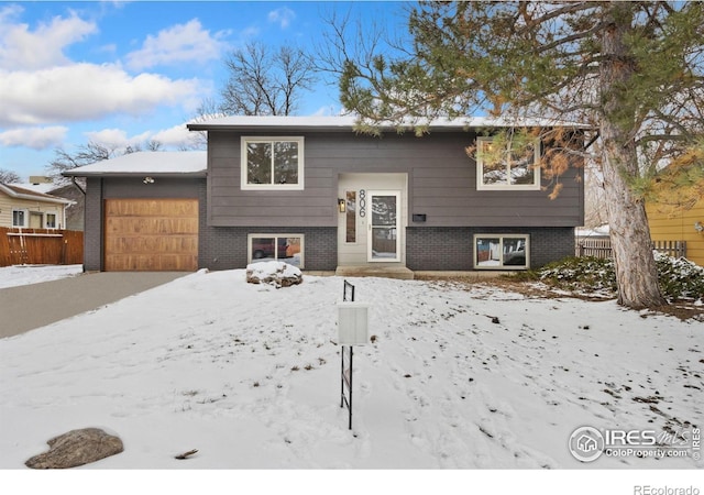 raised ranch with brick siding, an attached garage, and fence