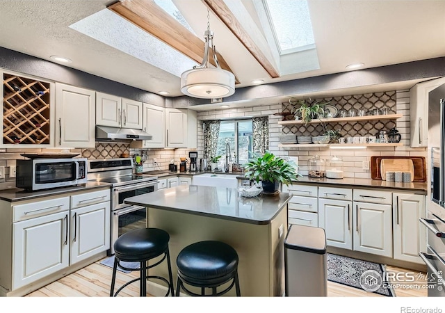 kitchen featuring appliances with stainless steel finishes, a center island, a kitchen breakfast bar, a skylight, and white cabinets