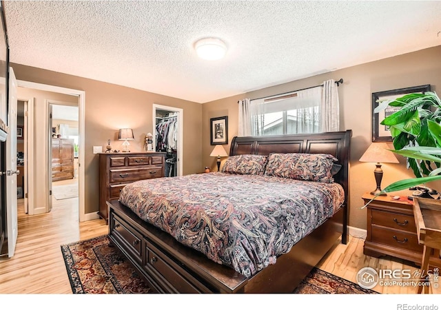 bedroom featuring light wood-type flooring, a closet, a walk in closet, and a textured ceiling