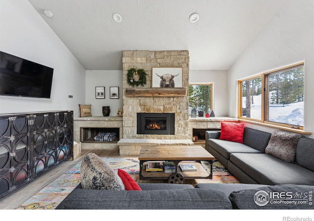 living room featuring a stone fireplace, vaulted ceiling, a textured ceiling, and light hardwood / wood-style floors