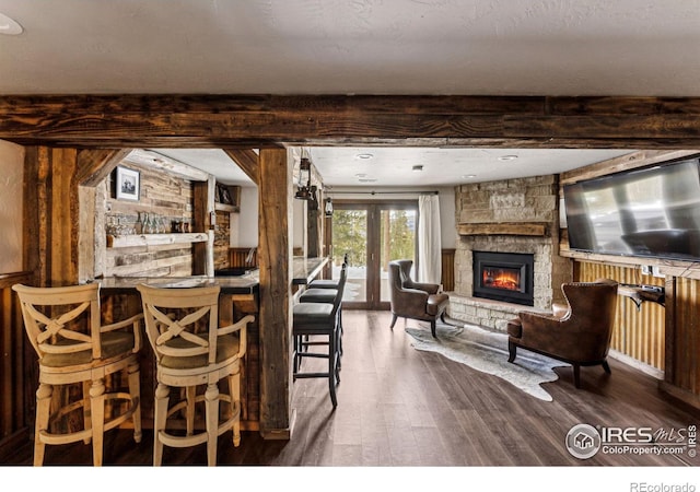 dining area with hardwood / wood-style flooring, bar area, beam ceiling, and a stone fireplace