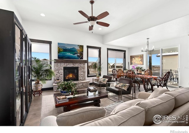 living room with a stone fireplace, light hardwood / wood-style floors, and ceiling fan with notable chandelier