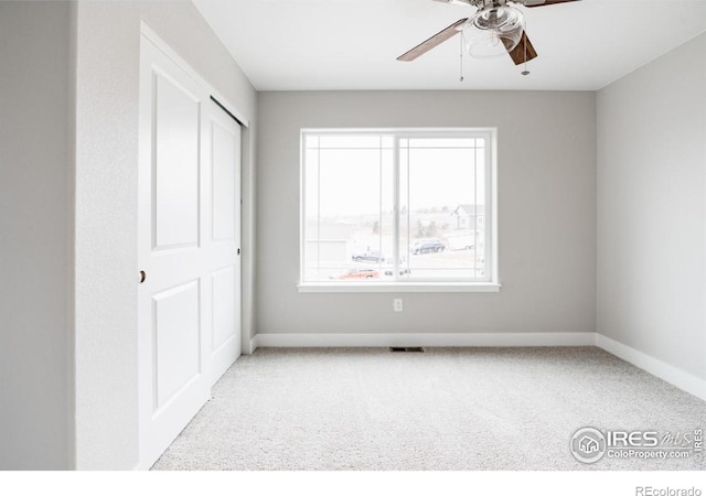 empty room with a ceiling fan, light colored carpet, visible vents, and baseboards